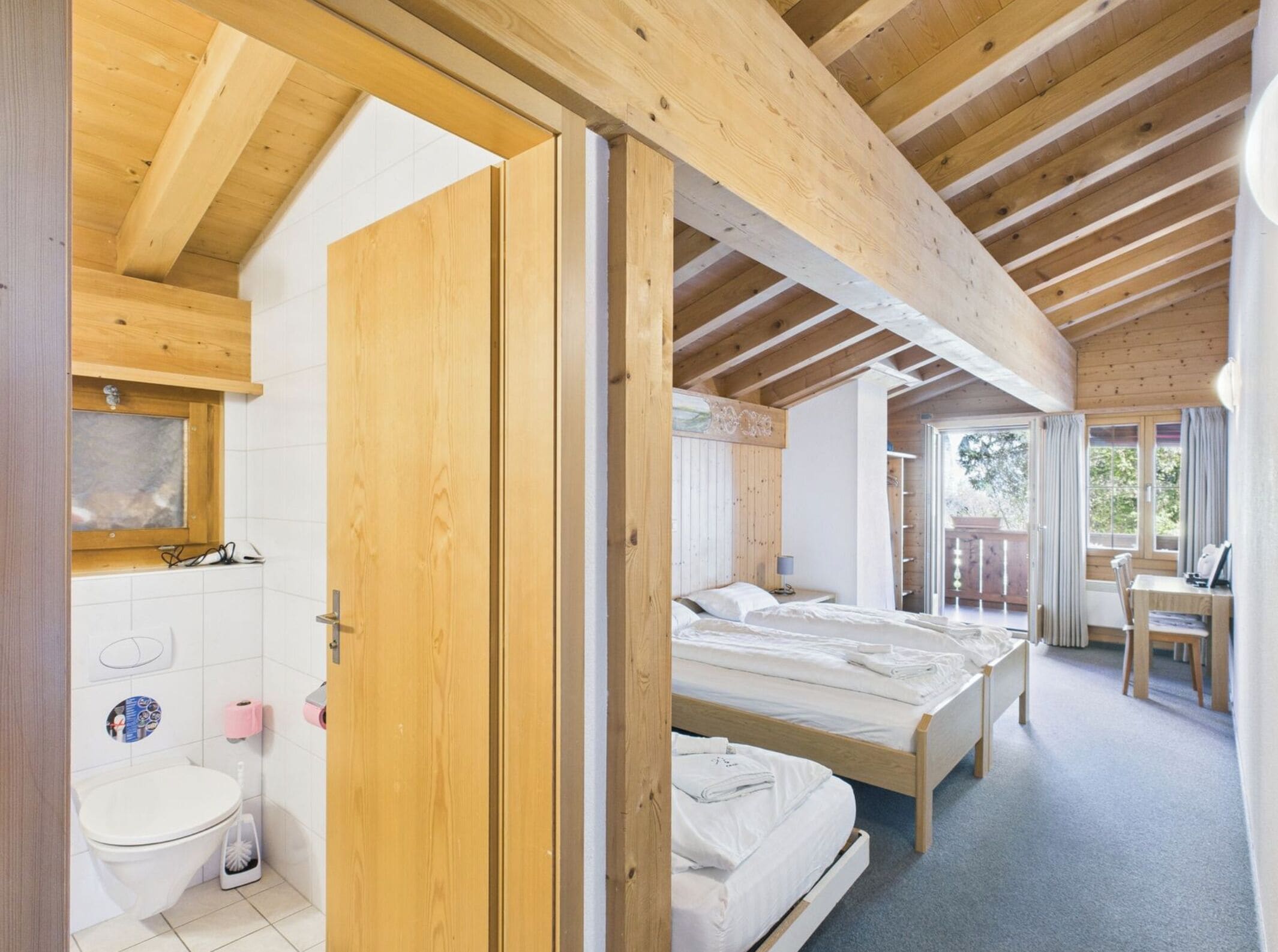 A wooden interior with a bathroom, two beds, and a dining area.