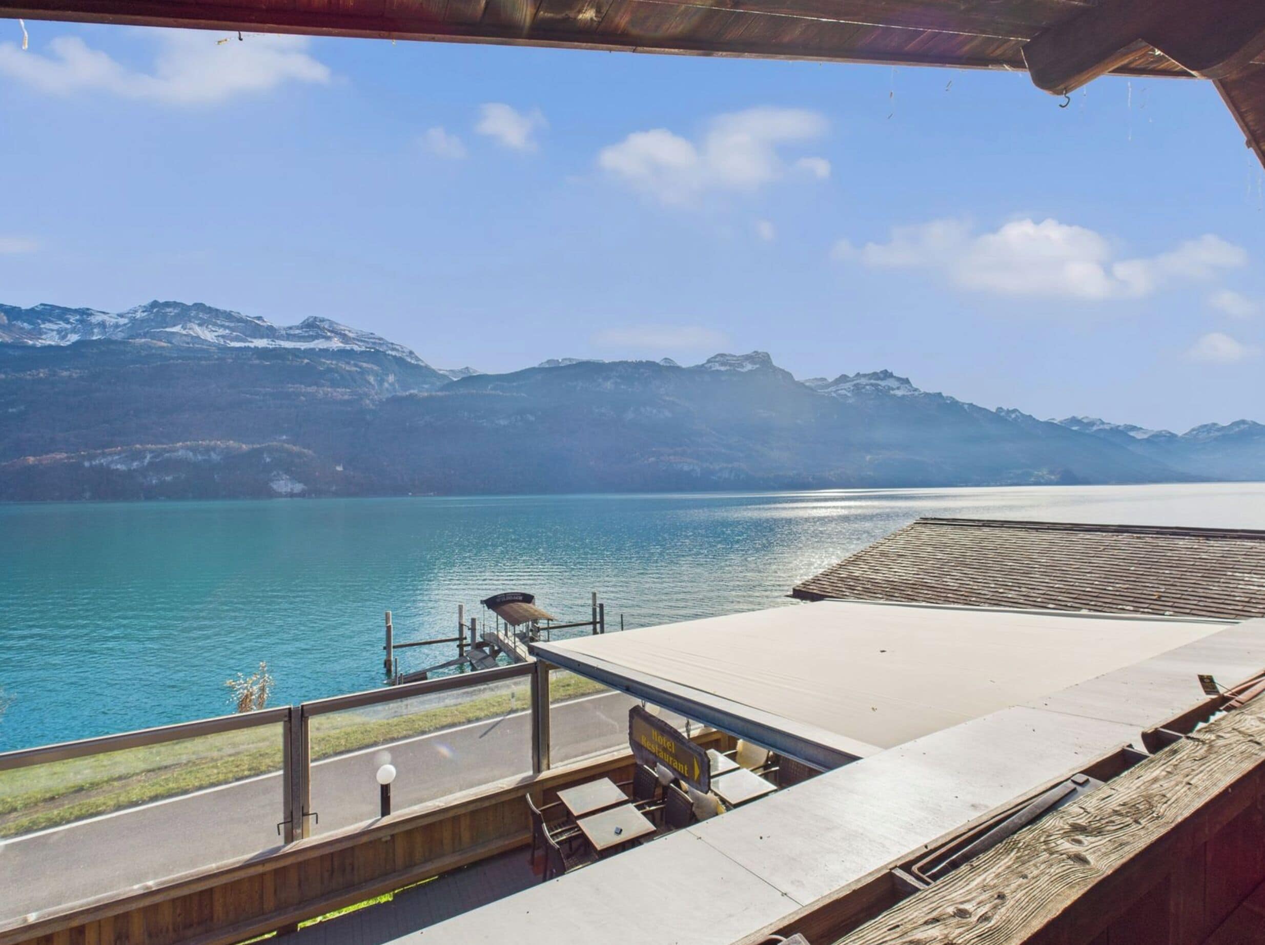 A lakeside view with a wooden deck, a sign for a hotel restaurant, and mountains in the background.
