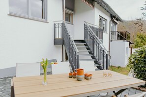 Une table en bois avec un vase et des tasses en céramique, un escalier et un bâtiment blanc doté de fenêtres.