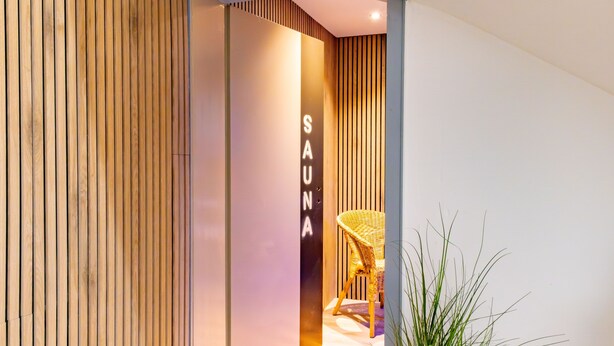 A spa entrance with a wooden slat wall, a sign reading 'SAUNA,' and a wicker chair.