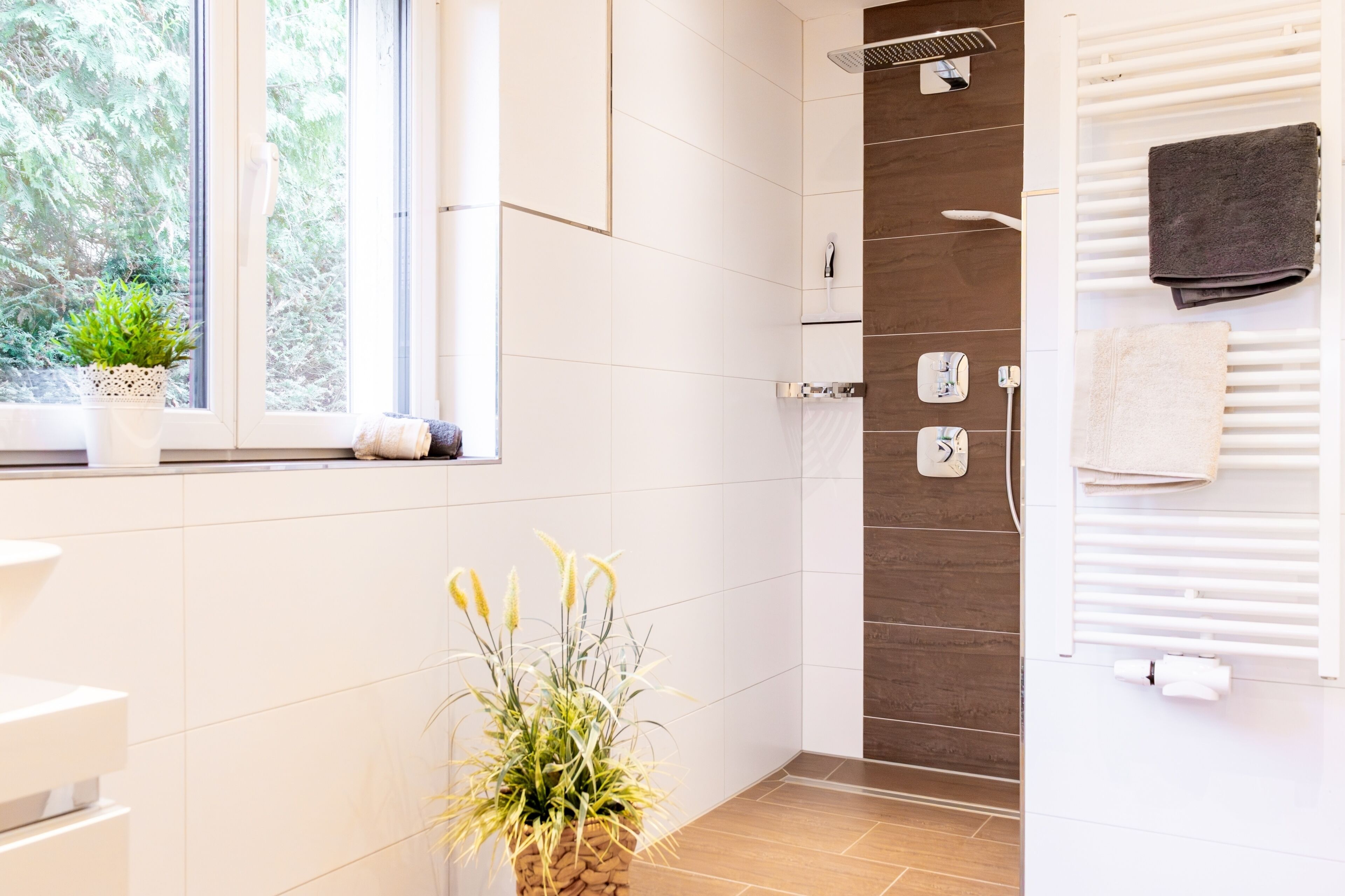A modern bathroom with a shower, a window with a plant, and a towel rack.