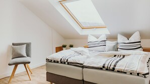 Een slaapkamer met dakraam, een bed met gestreept beddengoed, een stoel en een klein tafeltje met planten.