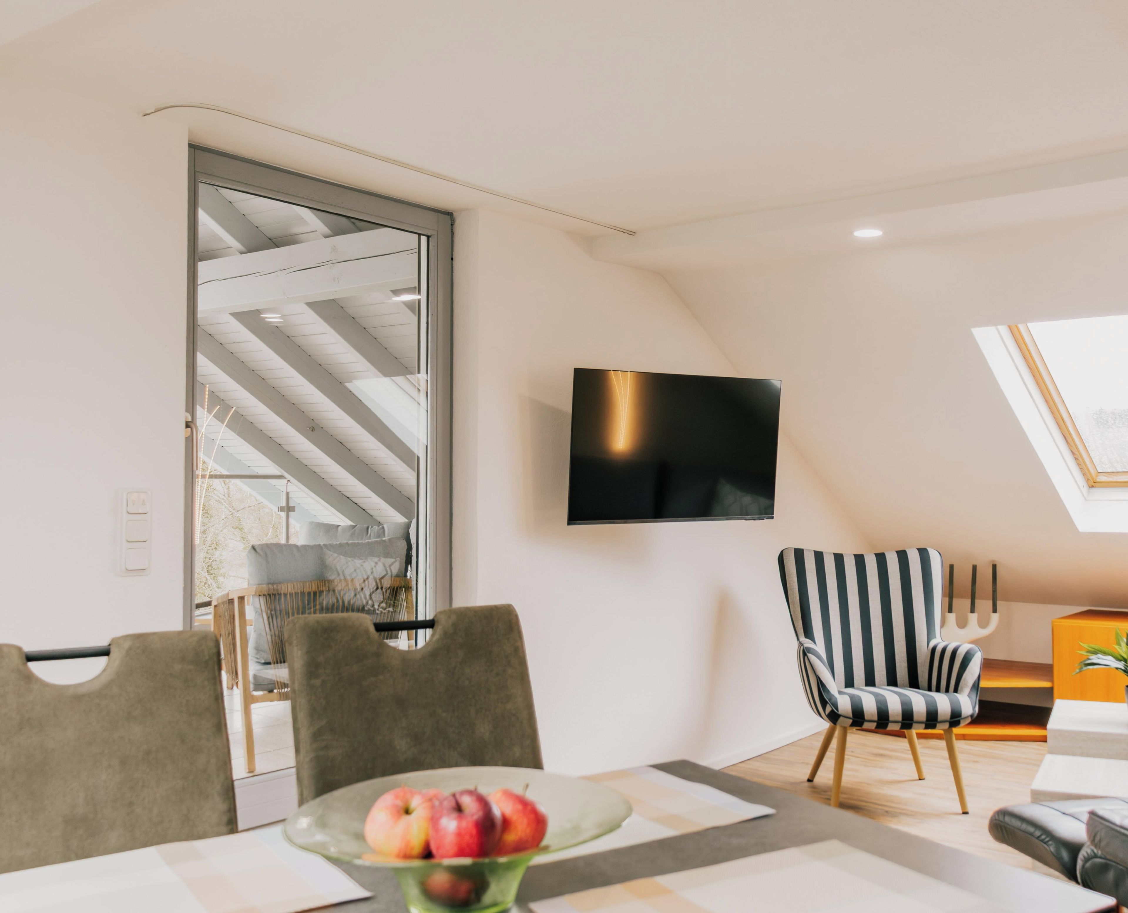Un salon moderne avec un téléviseur à écran plat fixé au mur, un coin repas comprenant une table et des chaises, et une grande fenêtre offrant une vue dégagée.