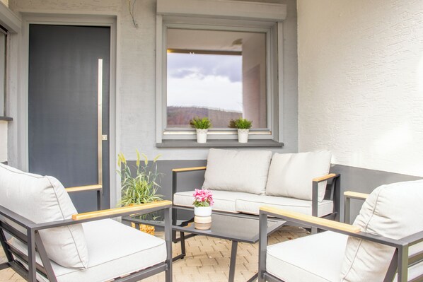 A patio with a sofa, two chairs, a small table, and two potted plants.