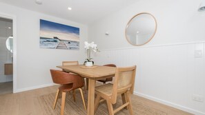 A dining area with a wooden table, four chairs, a vase with flowers, a wall-mounted mirror, and a painting of a pier. - Marina 14, Harrington (Harrington)
