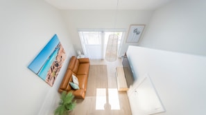 A spacious living room with a brown leather sofa, a large painting, and a hanging light fixture. - Marina 14, Harrington (Harrington)
