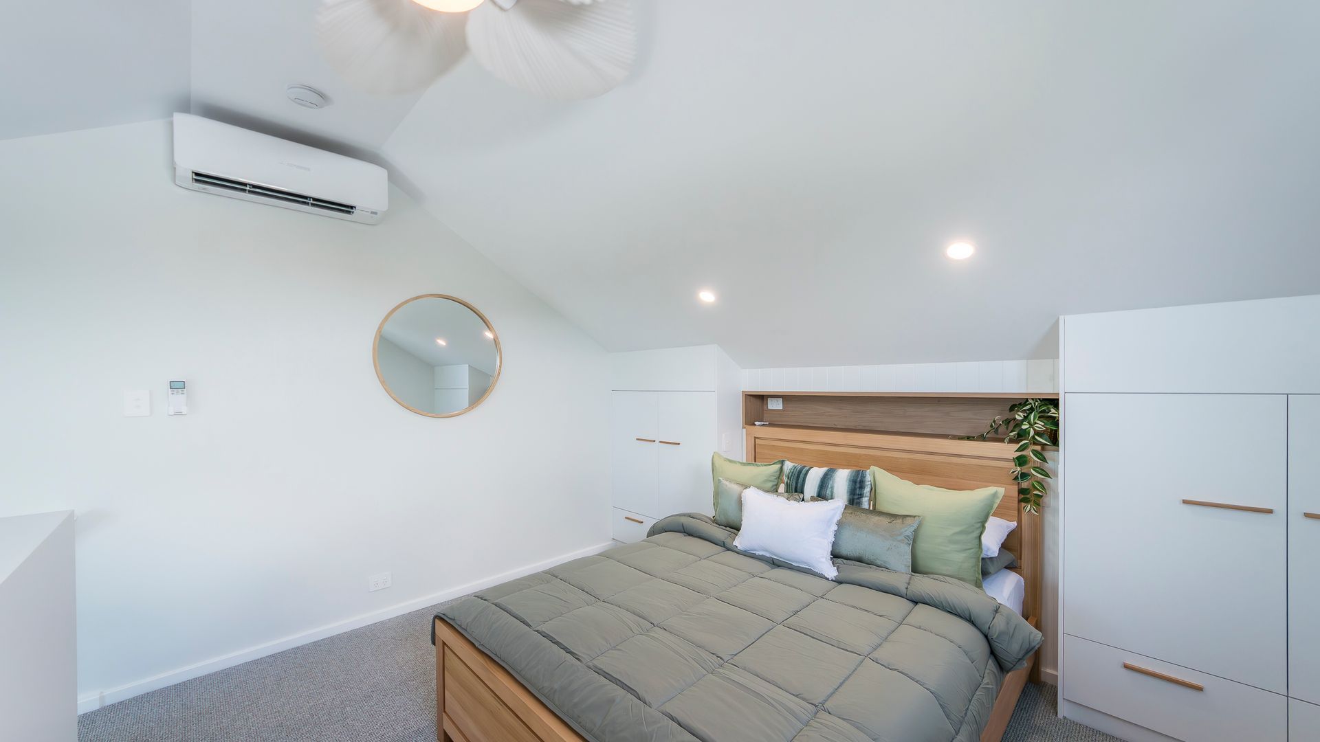 A bedroom with a bed, a round mirror, a wardrobe, and an air conditioning unit.