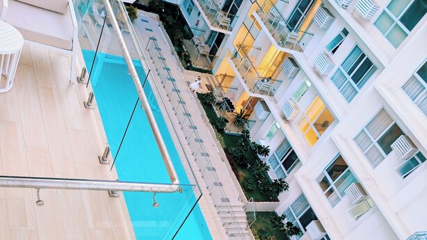 Una piscina en la azotea con barandilla de cristal, rodeada de edificios de varios pisos con balcones y espacios al aire libre.