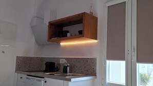 Una cocina compacta con lavavajillas, cafetera y un estante de madera sobre la encimera.