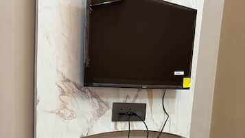 Et fladskærms-tv monteret på en marmorvæg, et brunt konsolbord med skuffer, en lampe og en lille pynteting.