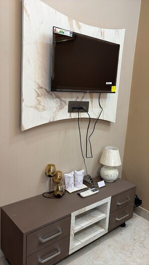 Un televisor de pantalla plana montado en una pared de mármol, una consola marrón con cajones, una lámpara y un pequeño objeto decorativo.