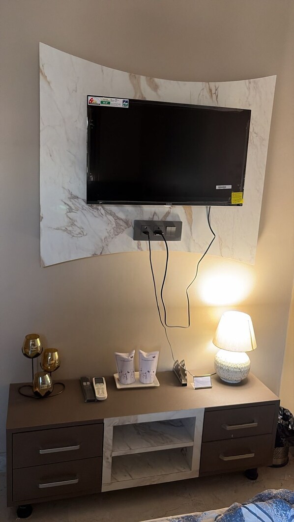 Una stanza con televisore a schermo piatto montato su una parete in marmo, una scrivania con lampada e un telefono.
