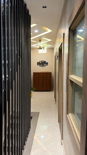 A corridor with a wooden cabinet, a glass door, and a ceiling with geometric lighting.