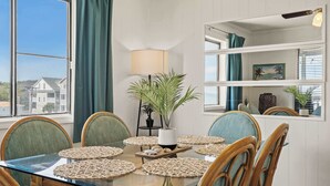 Un comedor con mesa de vidrio, individuales tejidos, sillas de mimbre, una planta en maceta y una lámpara.
