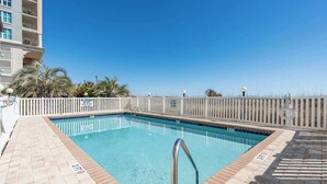 Piscina rectangular con escalera metálica, rodeada de una cerca blanca, y un cielo azul despejado arriba.