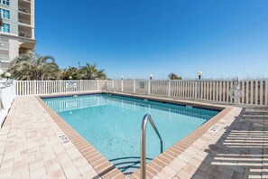 Ein rechteckiger Pool mit einer Metallleiter, umgeben von einem weißen Zaun, und einem strahlend blauen Himmel darüber.