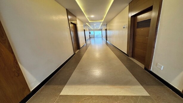 Un pasillo largo y estrecho con suelo alfombrado, puertas de madera e iluminación empotrada en el techo.