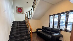 Una escalera con peldaños negros y barandillas de madera, un sofá de cuero negro y un ventanal con rejas de metal.
