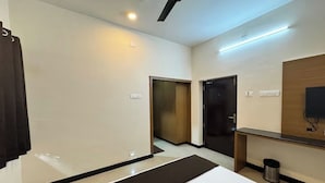 Habitación de hotel con cama, escritorio, espejo, televisor y puerta que da a otra habitación.