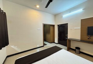 Habitación de hotel con cama, escritorio, espejo, televisor y puerta que da a otra habitación.