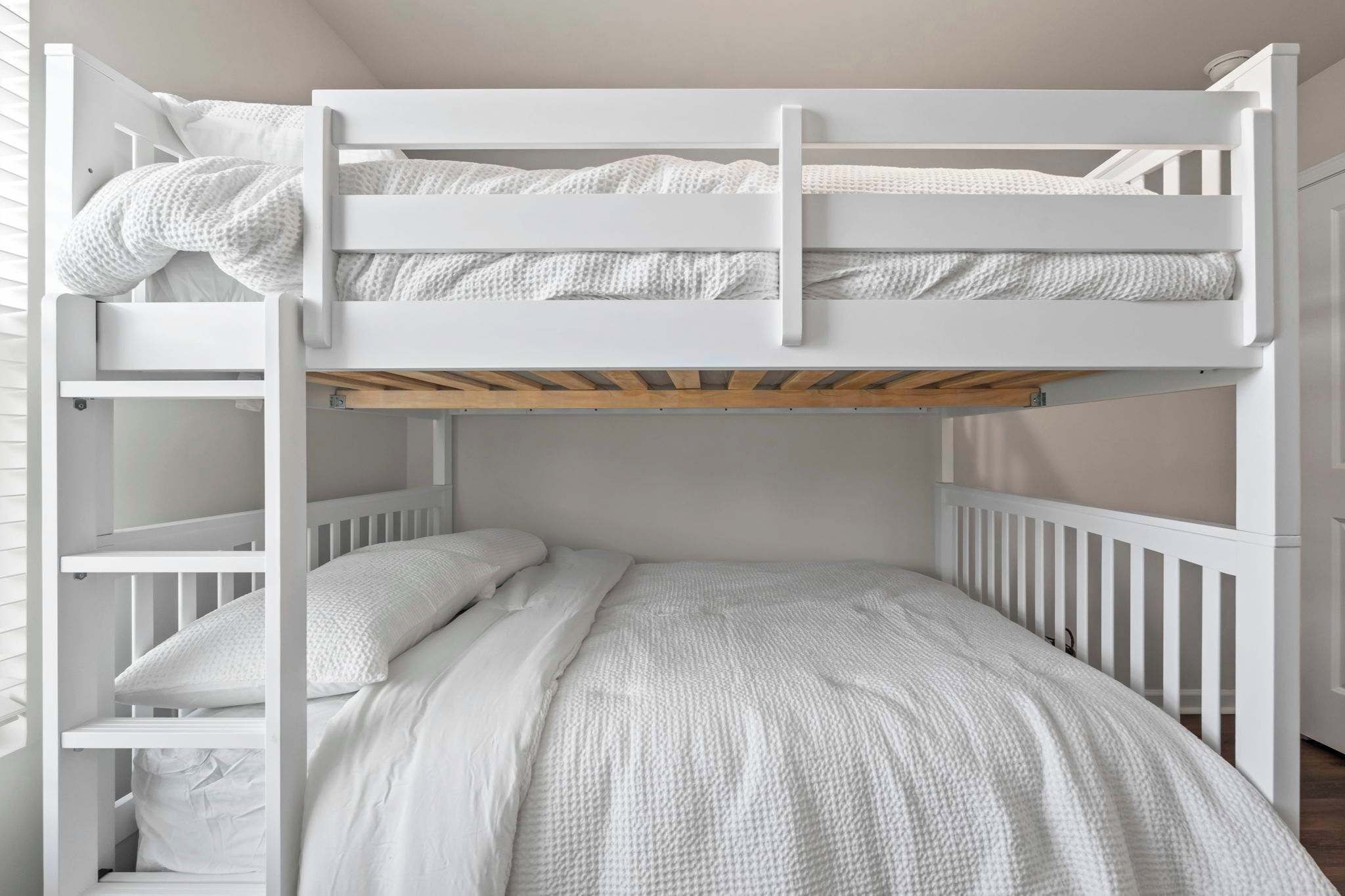 A bunk bed with white bedding and a wooden lower bunk.