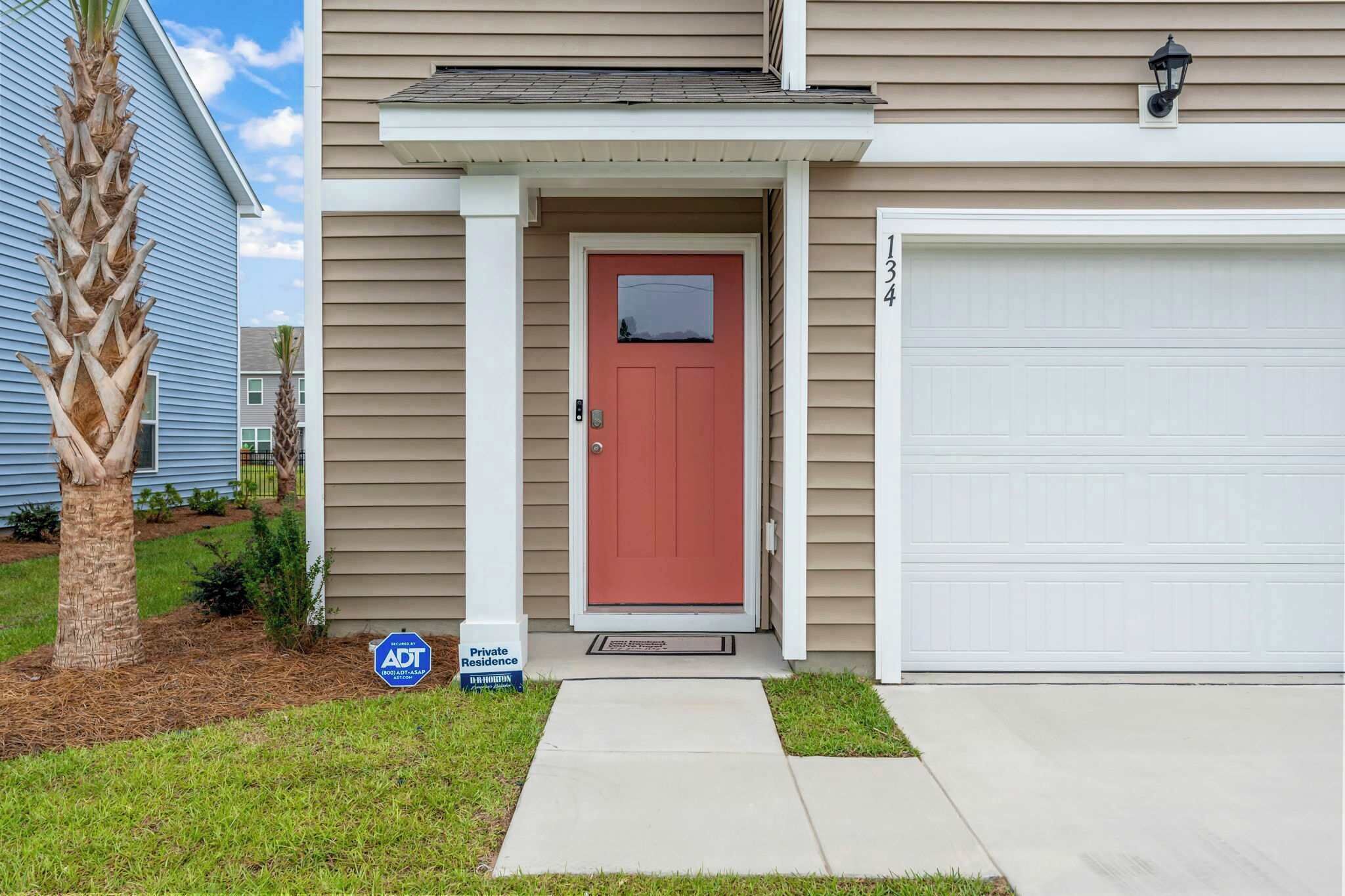 A residential house with a red door, a garage, and a palm tree in the yard.