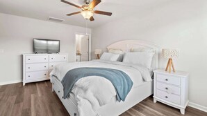 Een slaapkamer met een bed, nachtkastjes, een televisie, een plafondventilator en een lamp.