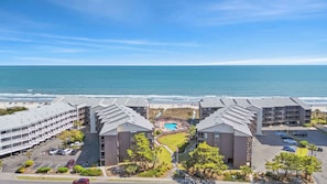 Ein Strandhotel mit mehreren Gebäuden, einem Schwimmbad und einem Parkplatz.