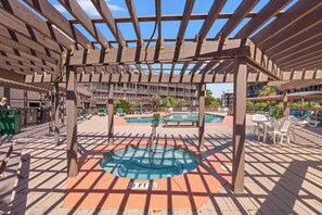 Eine Holzterrasse mit Pool, Liegestühlen und einer Pergola.