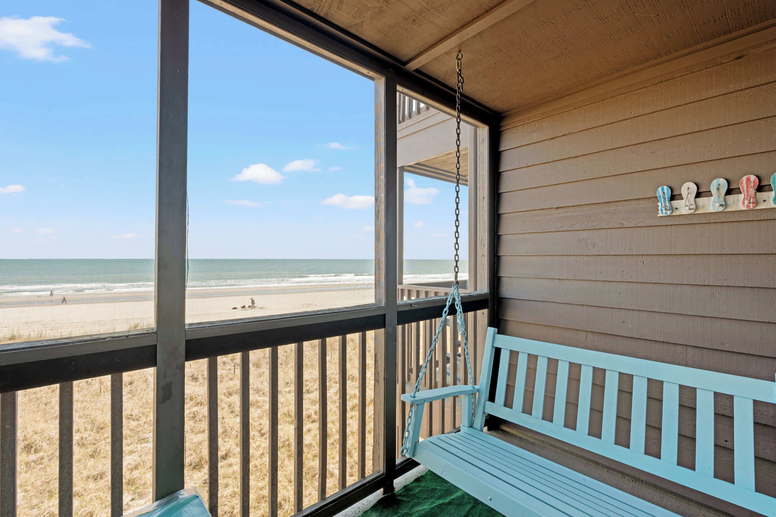 Eine Veranda mit einer Schaukel, Blick auf den Strand und eine Holzverkleidung mit Dekoration.
