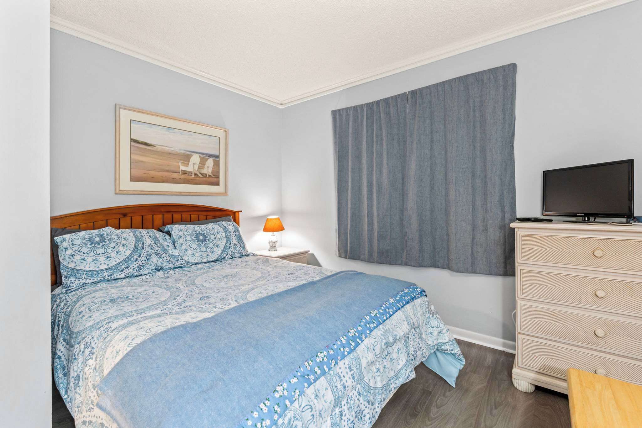 Quarto com cama, cômoda, televisão e um quadro na parede.