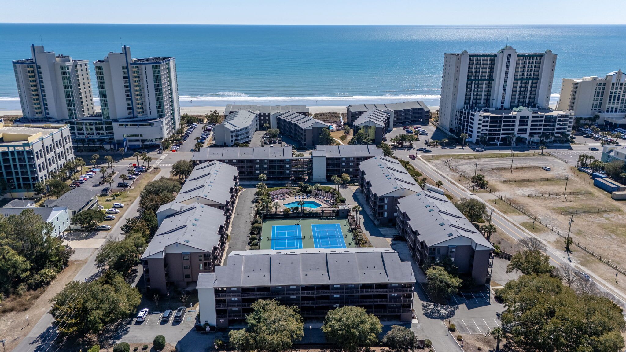 A coastal hotel complex with multiple buildings, a central pool area, and a view of the ocean.