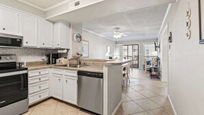 A kitchen with white cabinets, a dishwasher, a microwave, and an oven. There is a dining area with a table and chairs. - Orange Crush at Tilghman (North Myrtle Beach)