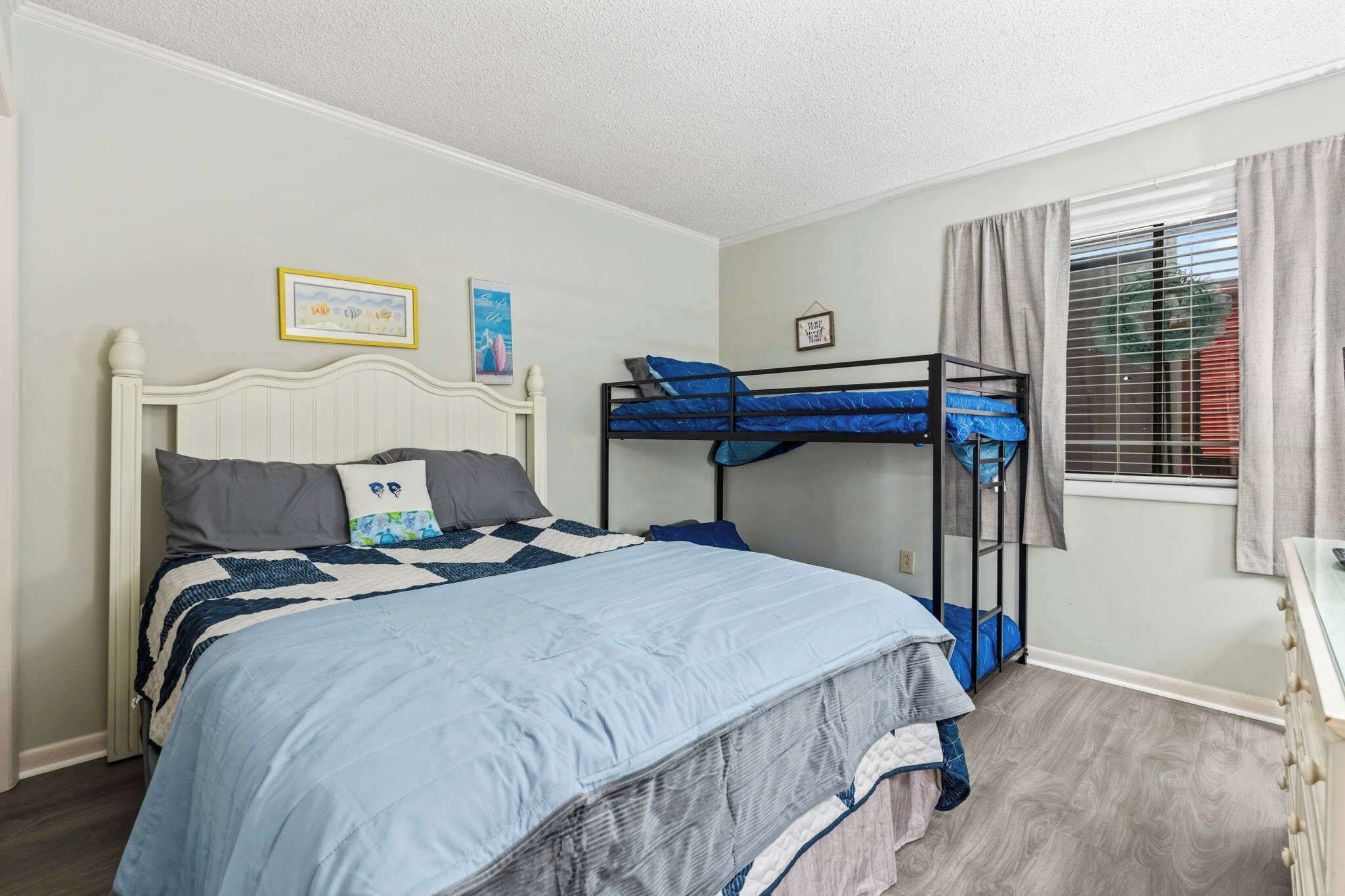 A bedroom with a bunk bed, a single bed, a dresser, and a window with curtains.