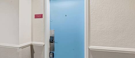 Una puerta azul con teclado numérico, marco blanco y pared texturizada de color blanco con el símbolo de número.