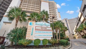 Schild für Beach Cove Resort mit einer Willkommensbotschaft, das Unterkünfte mit 1, 2 und 3 Schlafzimmern sowie Apartments direkt am Meer anzeigt.