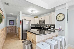 A kitchen with white cabinets, a black countertop, a stainless steel sink, a microwave, and a clock on the wall. - "The Pearl of Tilghman" (North Myrtle Beach)
