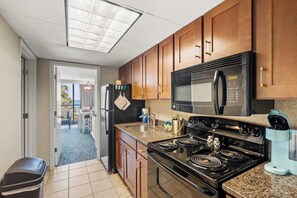 A kitchen with wooden cabinets, a black stove, a microwave, and a coffee maker. - "The Grand Coral" located coral beach (Myrtle Beach)