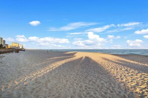 A beach with sand, a clear sky, and buildings in the background. - "The Grand Coral" located coral beach (Myrtle Beach)