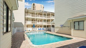 A pool area with a brick floor, blue lounge chairs, and a multi-story building in the background. - "Dreams By The Sea" at dunes village (Myrtle Beach)