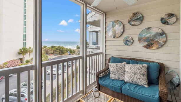 A balcony with a view of the ocean, a wicker sofa with cushions, and decorative plates on the wall. - "Soul Soother" at Tilghman (North Myrtle Beach)