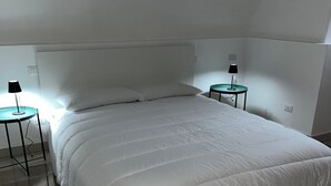 Ein ordentlich bezogenes Bett mit weißer Bettwäsche in einem Zimmer mit Fliesenboden und zwei Nachttischen mit Lampen.