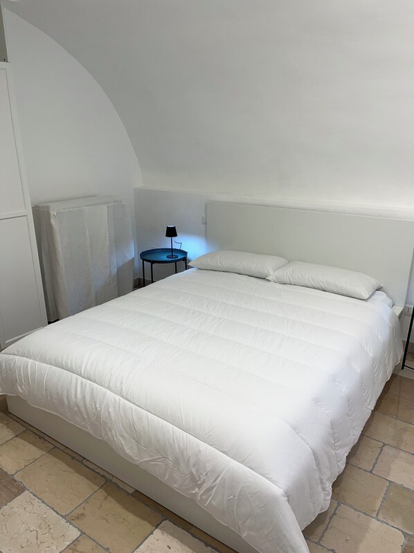 A bedroom with a large bed, a small side table with a lamp, and a radiator.