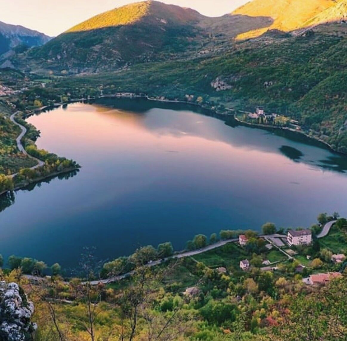 Ein See, umgeben von Hügeln, mit einigen Gebäuden in der Nähe des Ufers.