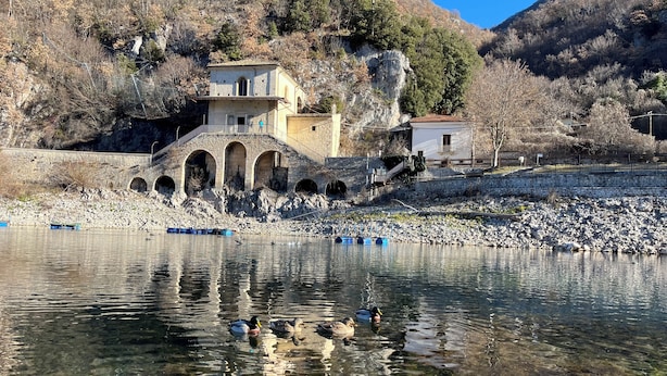 Eine Steinkonstruktion mit Bögen, ein Fluss und Gebäude im Hintergrund.