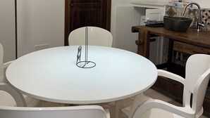 Ein Essbereich mit einem runden weißen Tisch, weißen Stühlen, einer Holztür und einer Küchenzeile mit Spüle und einer großen Schüssel.