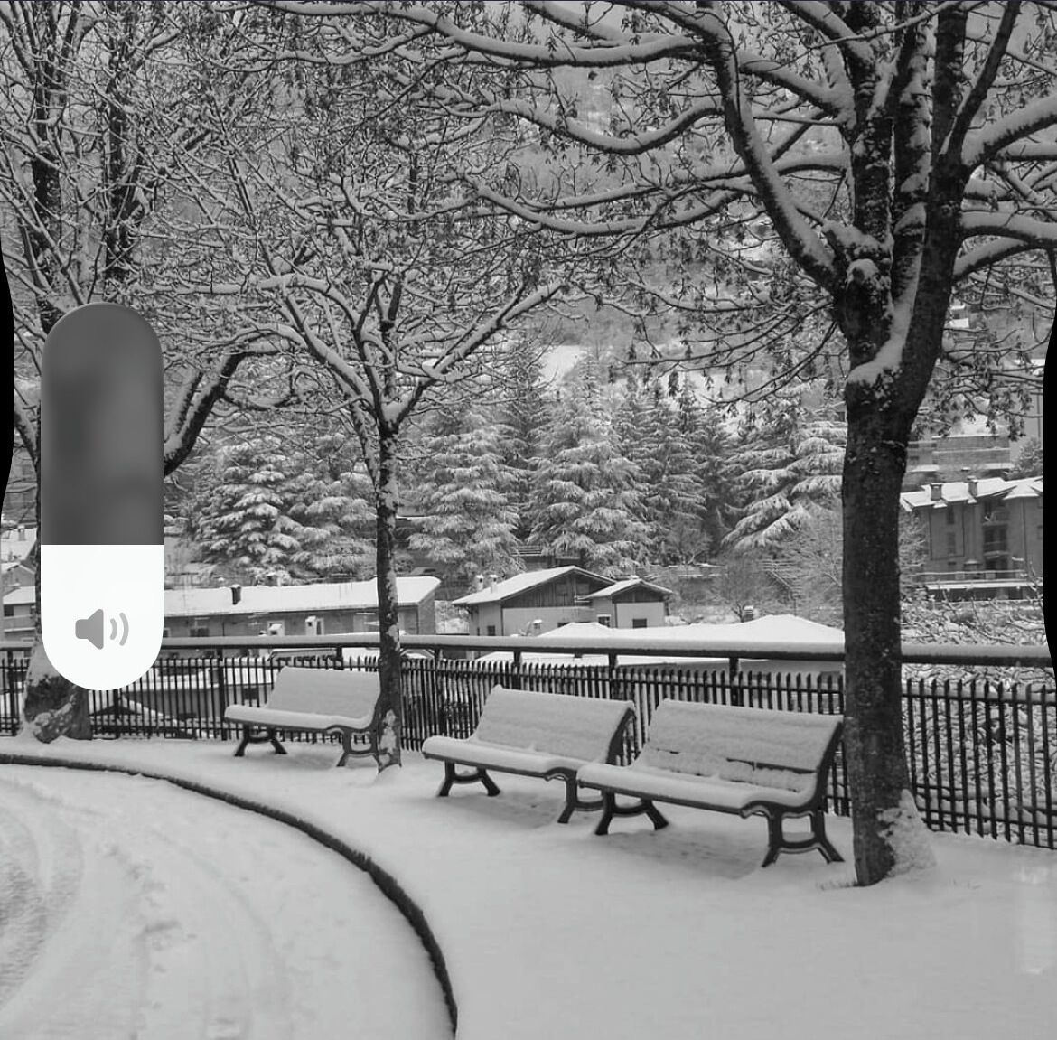 Ein mit Schnee bedeckter Park mit Bänken und einem Zaun.