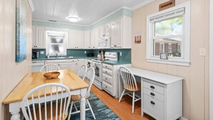 A kitchen with white cabinets, a wooden dining table, and a window with a view. - Coastal Cottage- 3 Bedroom (Surfside Beach)
