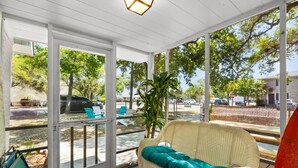 A covered outdoor seating area with a wicker sofa and chairs, a potted plant, and a view of the street. - Coastal Cottage- 3 Bedroom (Surfside Beach)