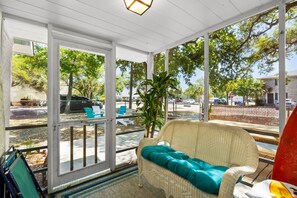 A covered outdoor seating area with a wicker sofa and chairs, a potted plant, and a view of the street.